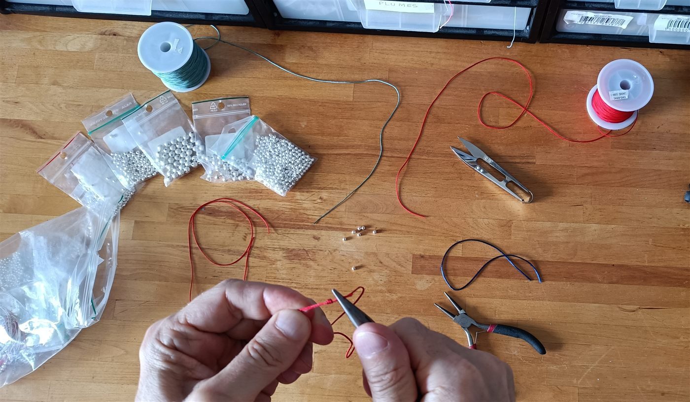 Nouage à la main d'un bracelet cordon rouge dans l'atelier RITES BIJOUX, perles en argent 925 sur l'établi